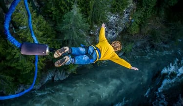 A person bungee jumping in a yellow shirt over a rushing river and green forest.