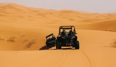 Adventure seekers driving black off-road buggy vehicles across golden Sahara Desert sand dunes.