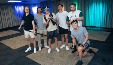 Group of young men, one man wearing a VR headset, one man holding an ice hockey stick