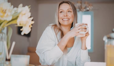 Smiling woman in a white shirt holding a coffee mug during a relaxed morning at home.