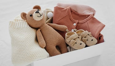 une boîte de vêtements rose pour bébé, chausson ourson et un ours en peluche