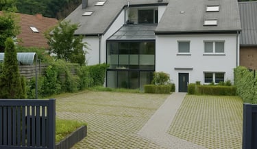 Maison moderne blanche avec grande véranda en verre et allée pavée entourée de verdure.