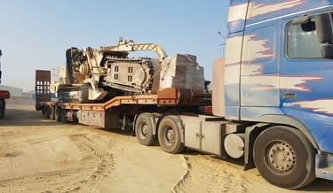 تريلا لوبد زرقاء تحمل حفارًا كبيرًا بلون البيج/البني الفاتح، وهي جاهزة لخدمات نقل معدات ثقيلة.