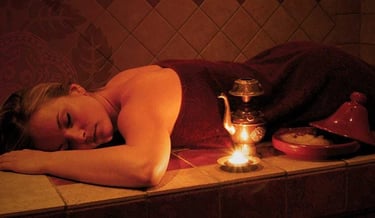 A woman lying down on a hammam table enjoying a moment of relaxation while closing her eyes