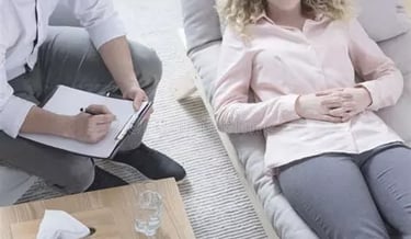 Femme allongée en relaxation mains sur le ventre à côté de son thérapeute qui prend des notes