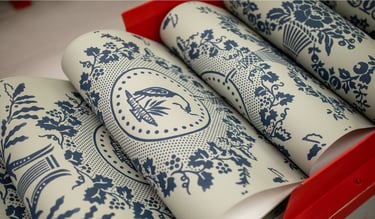 Rolls of vintage blue and white toile wallpaper with floral and bird patterns in a red rack.