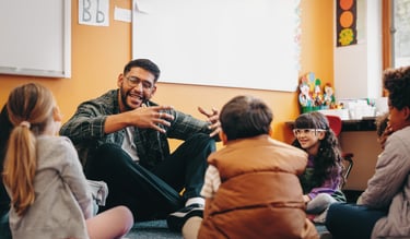 A teacher sitting on the floor with a small group of students in a classroom.