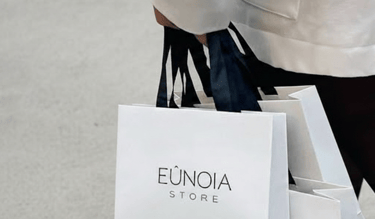Una persona camina mientras lleva bolsas de compras de lujo blancas de Eunoia Store con asas negras.