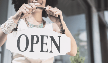 Photo of a small business owner smiling while holding an "open" sign