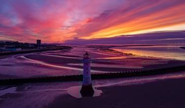 Aerial view of Perch Rock Lighthouse on New Brighton beach at sunset with purple sky.