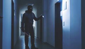 Intruder in a dimly lit hallway carrying a crowbar and flashlight, emphasizing the importance of ala