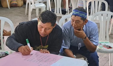 Two indigenous men in a workshop collaborating and writing on a pink poster at a community meeting.