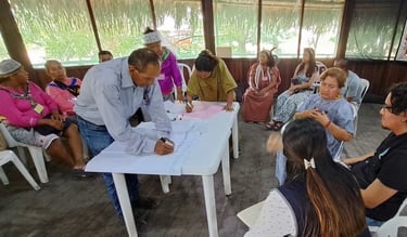 Indigenous community leaders participate in a collaborative workshop, signing documents on a table during a meeting.