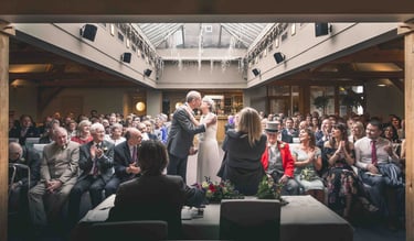 A bride and groom sharing their first kiss during a modern indoor wedding ceremony surrounded by guests.
