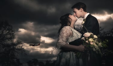 A bride and groom sharing a romantic kiss under dark storm clouds with a plane flying in the background.