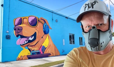 man in pup half-mask in front of a wall mural of a podcast dog