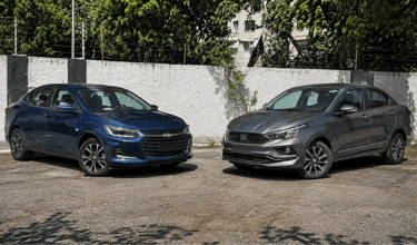 Chevrolet Onix Plus e Fiat Cronos em perspectiva 3/4, posicionados frente a frente.