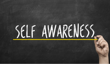 a hand holding a pencil and writing self - awareness on a chalkboard