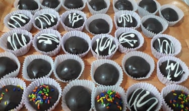 A tray of homemade chocolate truffles with white icing drizzle and colorful sprinkles in white paper liners.