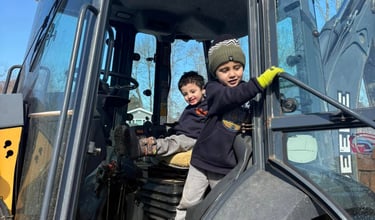 Two young boys playing inside the driver's cab of a yellow John Deere construction tractor.
