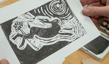 A handmade black and white linocut print of a running hare under a full moon.