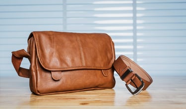 Vintage travelling for men's accessories, brown bag and belt put on modern wooden desk table in the office