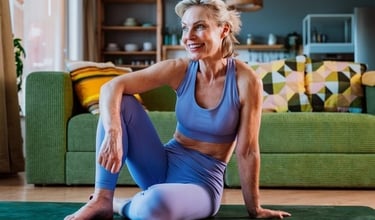 Smiling senior woman in activewear sitting on a yoga mat in her bright living room, enjoying a post-workout moment.