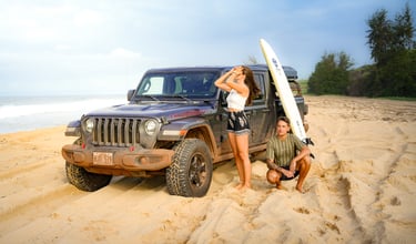 a man and woman standing in front of a jeep on the beach