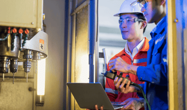 two men in hard hats and hard hats are standing in front of a machine