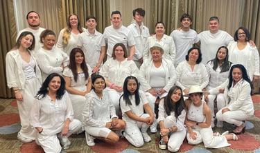 A large multi-generational group of people posing for a photo wearing all-white clothing at an event.