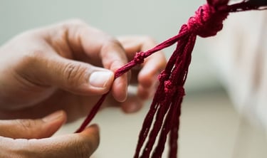 manos atando intrincados nudos de macramé rojo para un proyecto de artesanía textil hecho a mano