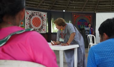 Indigenous woman writing at a community workshop featuring traditional textiles and cultural art.