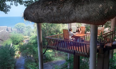 A couple having a romantic dinner in a treehouse-style balcony overlooking tropical greenery