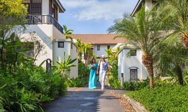 A couple walking down a tropical resort pathway lined with lush greenery, ferns, and palm trees