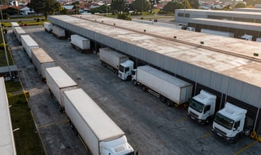 Overhead wide view of Medellín logistics hub at dawn, modern freight trucks lined at loading docks, clear sightlines across the facility, natural daylight, operational scale visible
