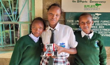 3 kenyan girls in school uniforms, holding a robot