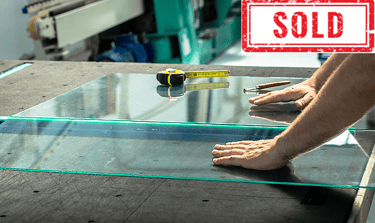 Worker measuring and handling glass sheet on a table, labeled "SOLD".