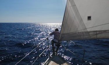 Un hombre sentado en la proa de un velero, con la vela a su espalda, navegando