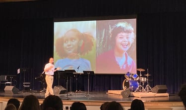 a man standing on a stage with a video screen showing a video of a woman