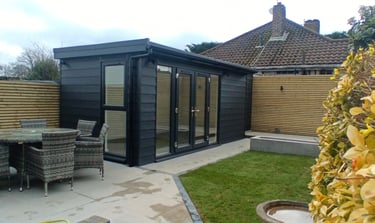 Modern black garden room with french glass doors next to a patio dining set and lawn.