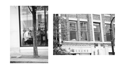 Black and white street photography of a person sitting in a cafe window next to a brick building.