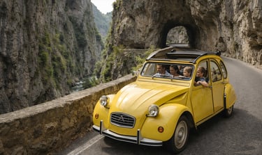 A family in a classic yellow Citroen 2CV driving through a scenic mountain gorge road.