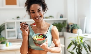 A smiling woman in fitness wear enjoying a healthy fruit and yogurt bowl for a nutritious breakfast.