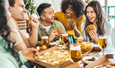A diverse group of happy friends eating pizza and burgers with craft beer at a restaurant table.