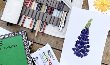 a bunch of art supplies: watercolour, pencil, brushes, paper on the table