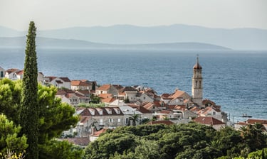 Panoramic view of Sutivan with red-tiled roofs and a historic church tower by the Adriatic Sea.