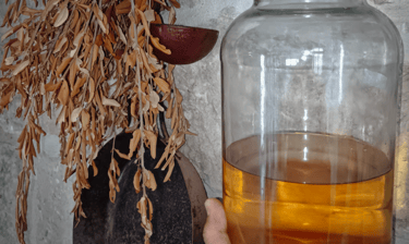 A glass jar of rakija next to dried olive branches and rustic kitchenware.