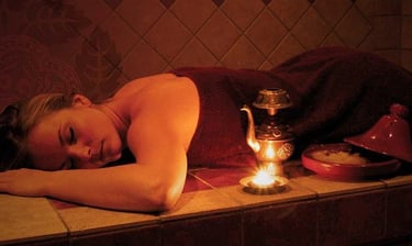 A woman lying down on a hammam table enjoying a moment of relaxation while closing her eyes