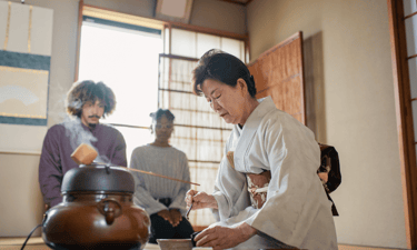 woman wearing a kimono performs tea ceremony and tourists watching in the back