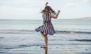 Fashion photography - a girl in a striped dress dancing on the beach